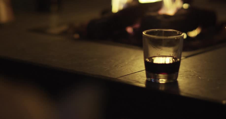 A shot glass with dark liquid next to a fireplace