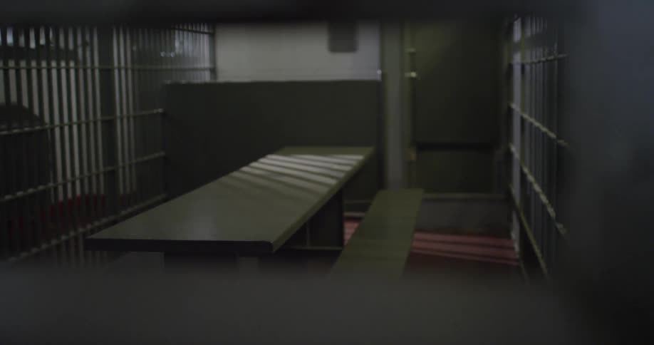 Looking through bars at a prison area with a table and bench in the center