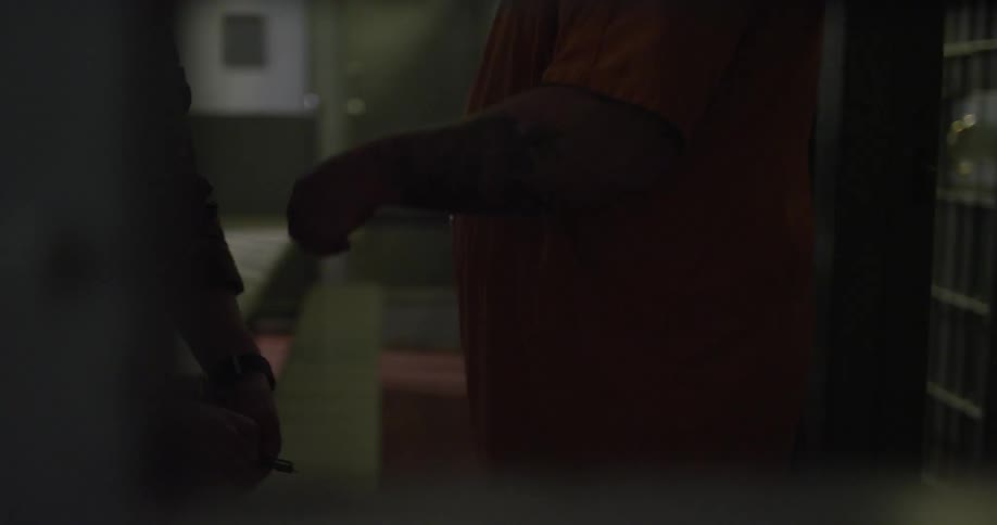A prisoner has his handcuffs removed in a dark area