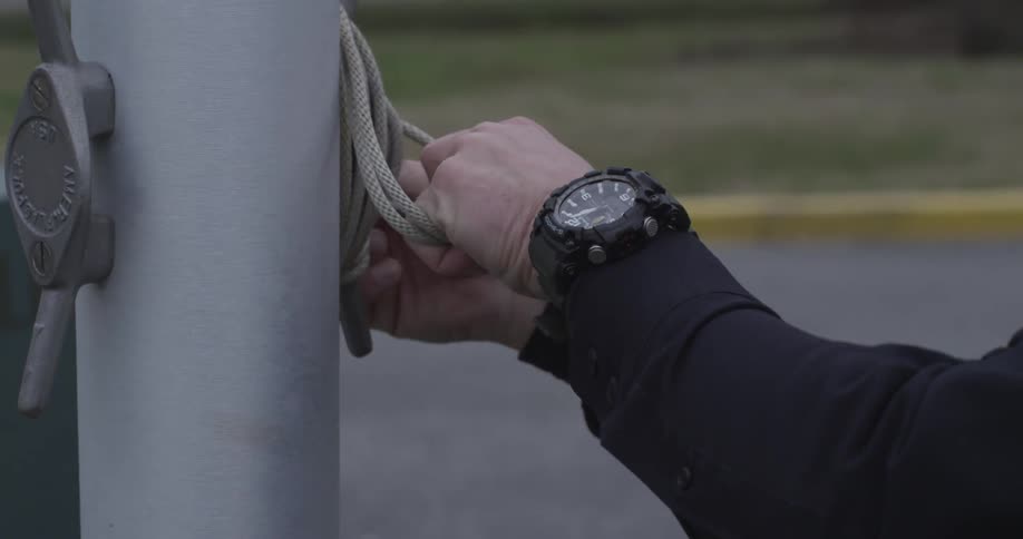 A man is tying a knot on a flagpole