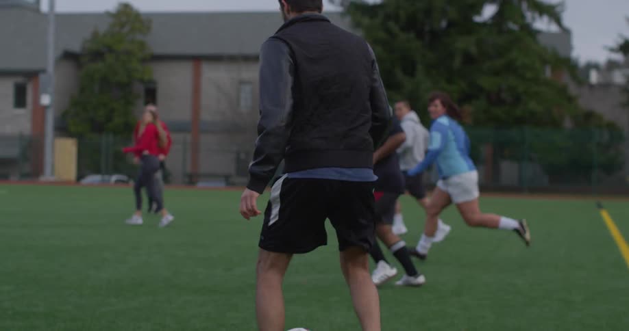 Men and women play soccer on a field on a cloudy day