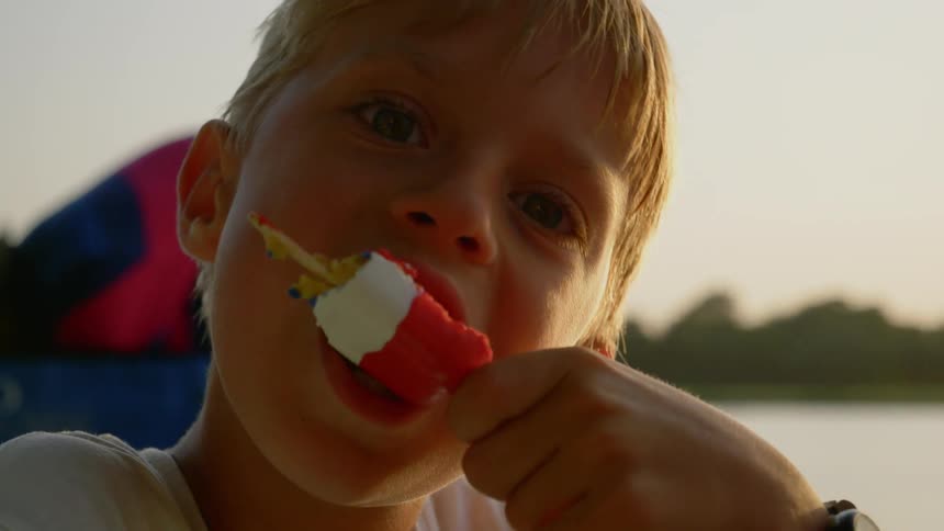 Blonde toddler boy eats ice cream at sunset