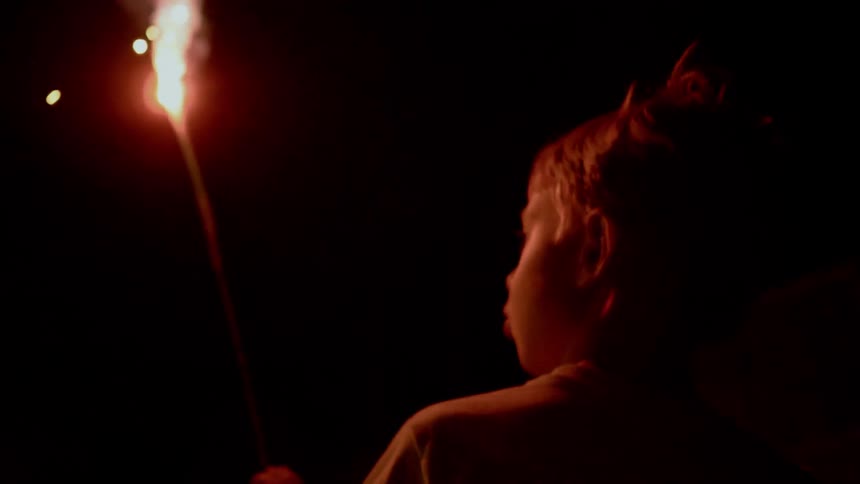 A little boy runs outside at night holding a flaming stick