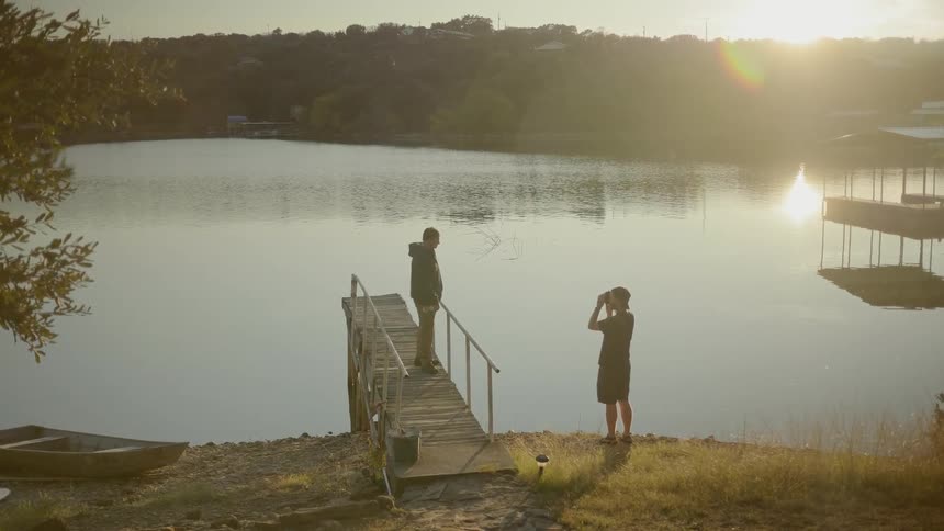 A man taking a photo of another man standing on a pier at a lake