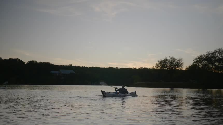 A man rows a kayak on a lake at sunset