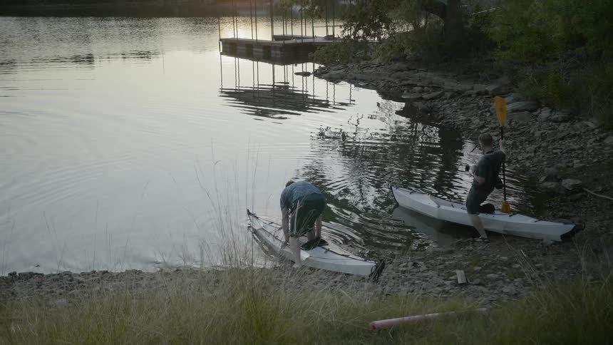 A group of men climbing into a pair of kayaks on a lake shore