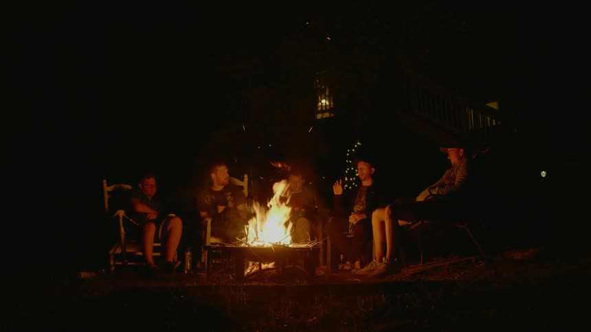 A group of young men sit around a fire pit and talk