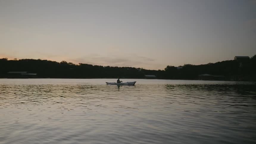 A person paddles a kayak on a lake at sunset