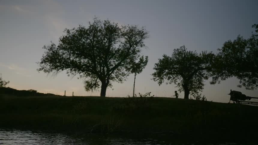 Kids run through the grass near a lake at night