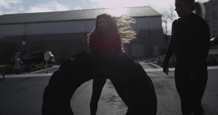 Two women flip a large tire outside