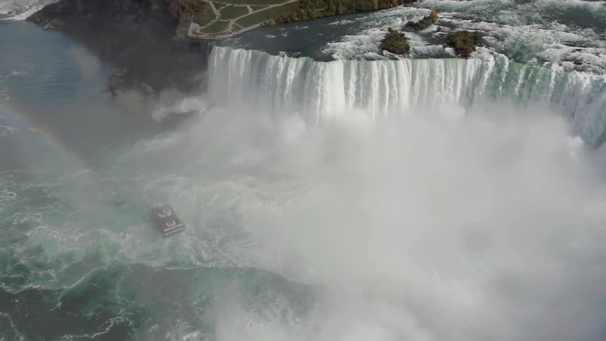 Rainbow shines over boat skirting large waterfall near city