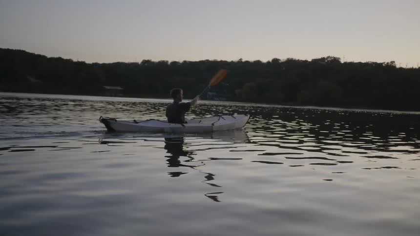 Man paddles canoe toward forested shoreline