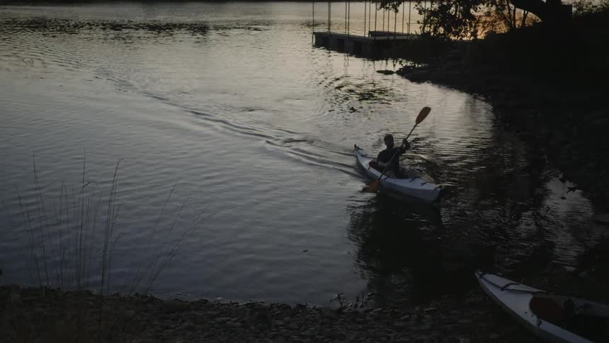 A man in a kayak paddles into the shore when dusk is turning to night