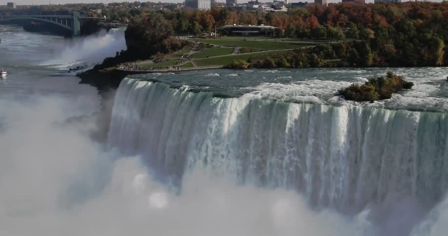 Water rushes down a large cliff as mist rises from the river below