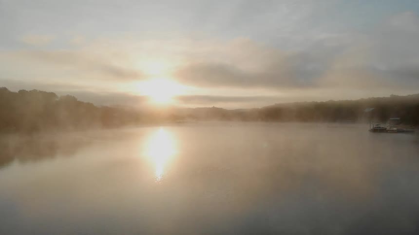Mist lays over lake and forest as sun rises on the horizon
