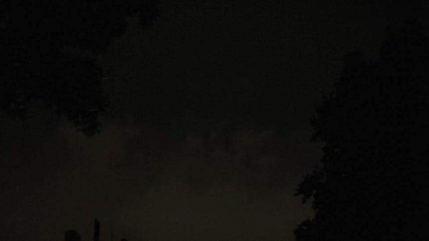 Lightning strikes behind a covering of clouds illuminating the sky over a building briefly