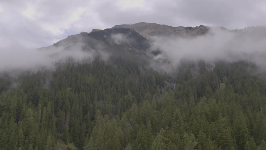 Clouds hover above a forest at the base of a mountain