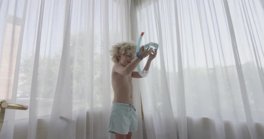A young boy plays with a snorkel and takes it off of his head