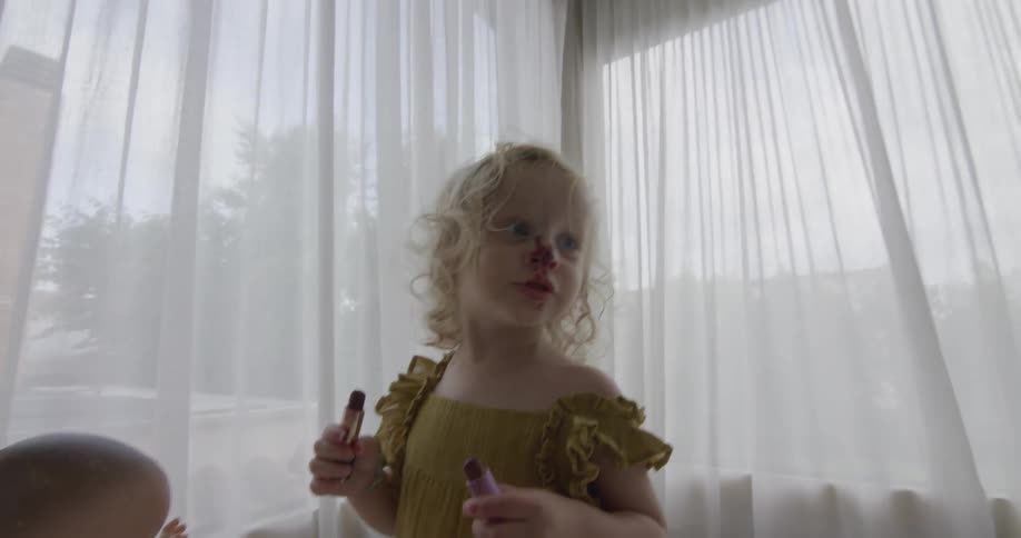 Young girl plays with lipstick and a doll in curtained room