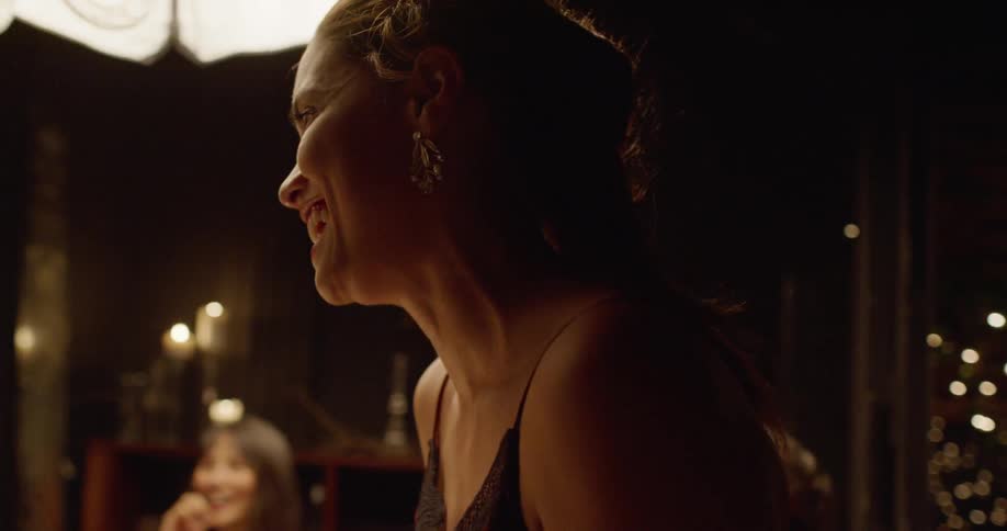 Woman sitting at the dinner table laughs and talks to the people in a restaurant at night