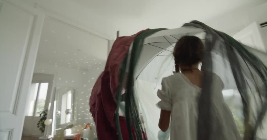 Young girl jumps up and down as she holds an umbrella covered with pieces of fabric