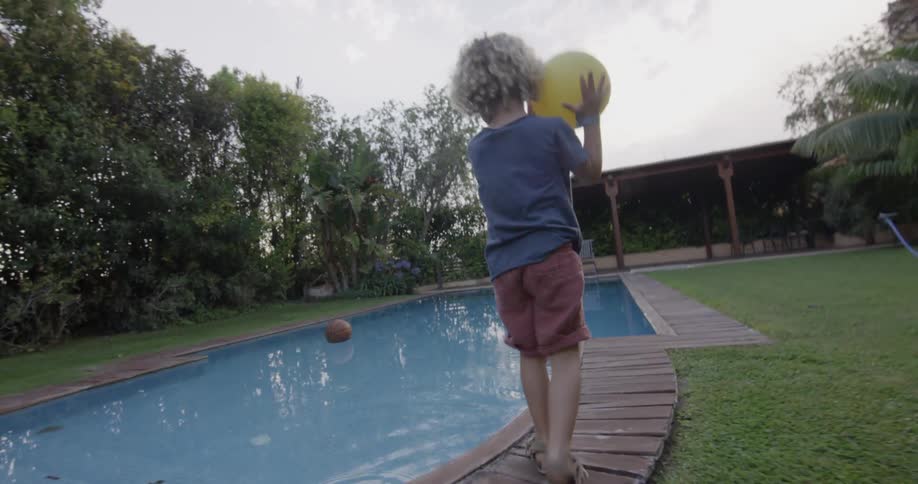 Two young children run to an inground pool and throw a pool into it