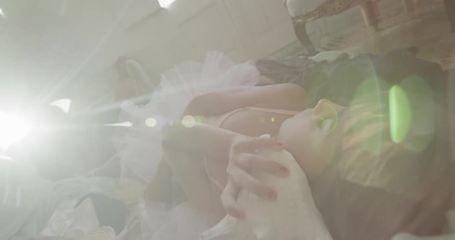 A girl in a tutu lays on the ground with a seashell at her ear