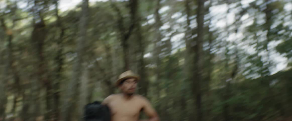 A shirtless man running in the forest carrying a backpack