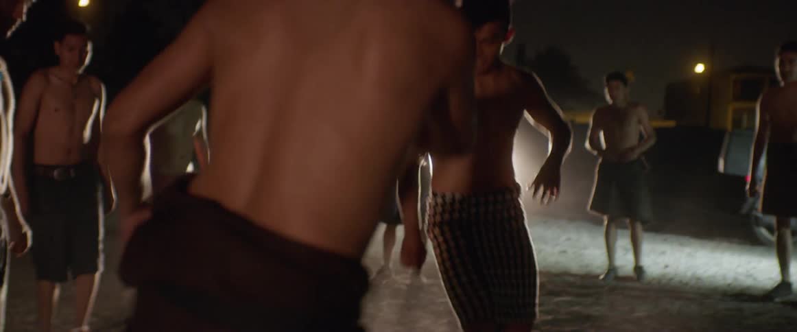 A group of men dance around in a circle at night lit by car headlights