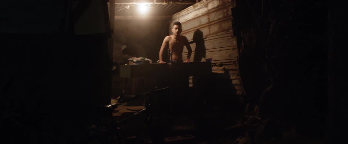 A man stands in a small shack illuminated be a single light bulb