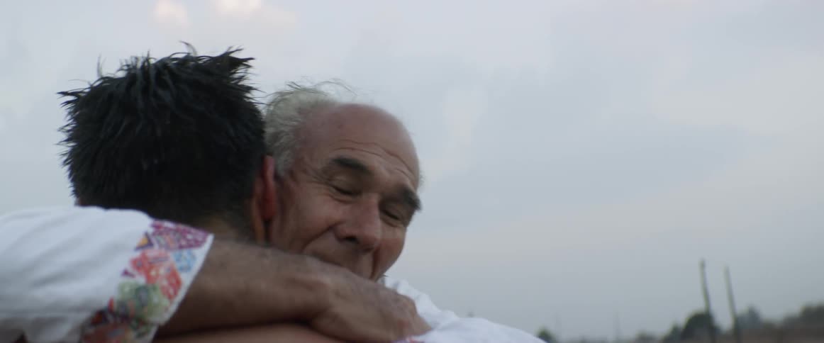 An elderly man hugging a shirtless younger man