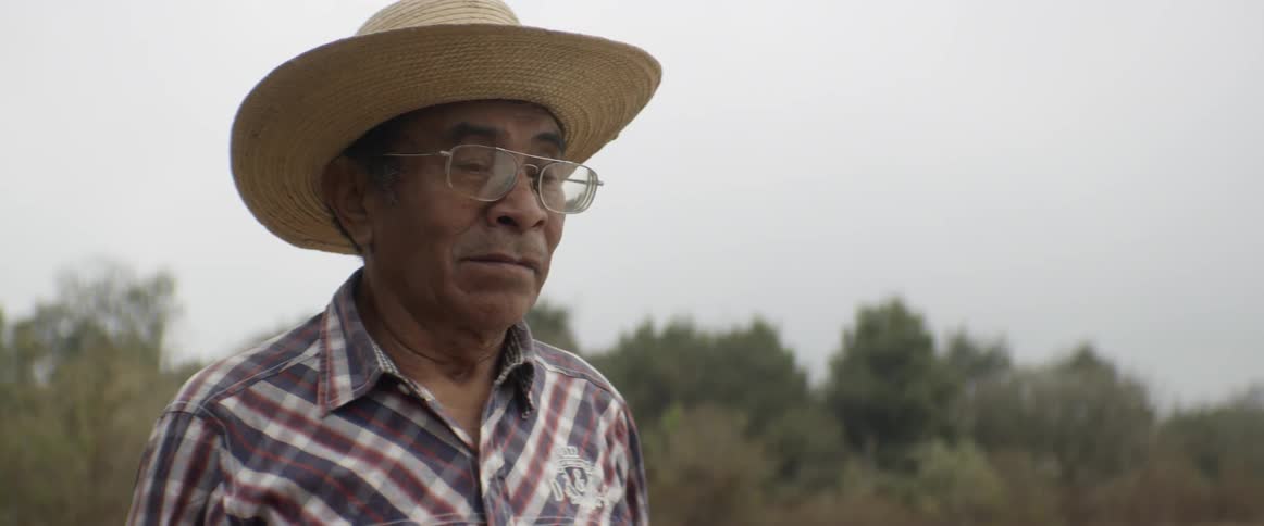 A native man wearing a flannel shirt and a woven straw hat