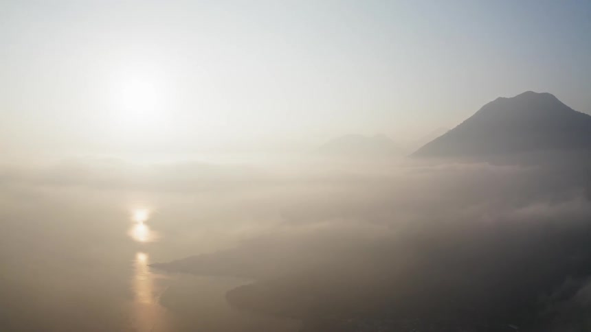 The sun shines through the fog above the sea