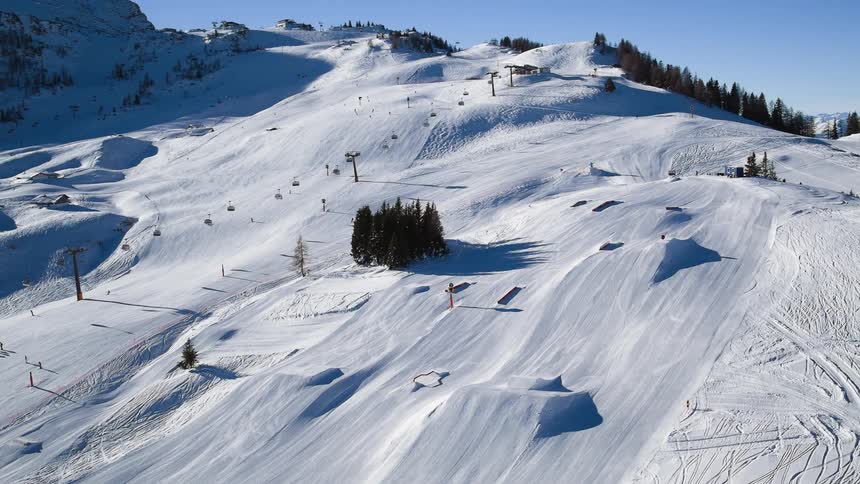 Ski lifts travel up and down the snowy mountain under a blue sky