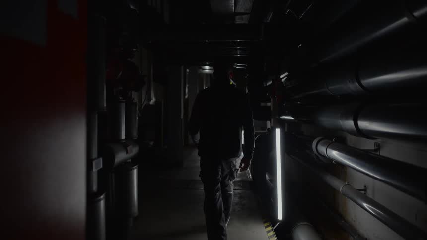 Man walks down dimly lit corridor lined with pipes