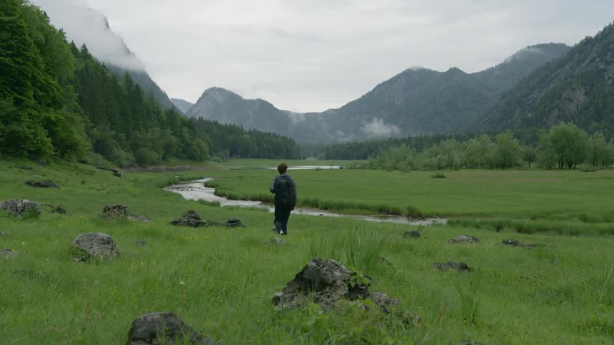 A person walks across a field towards a river