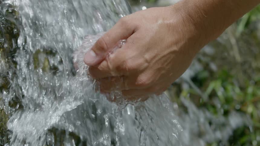 Man cupping his hands to gather water thats flowing heavily outdoors