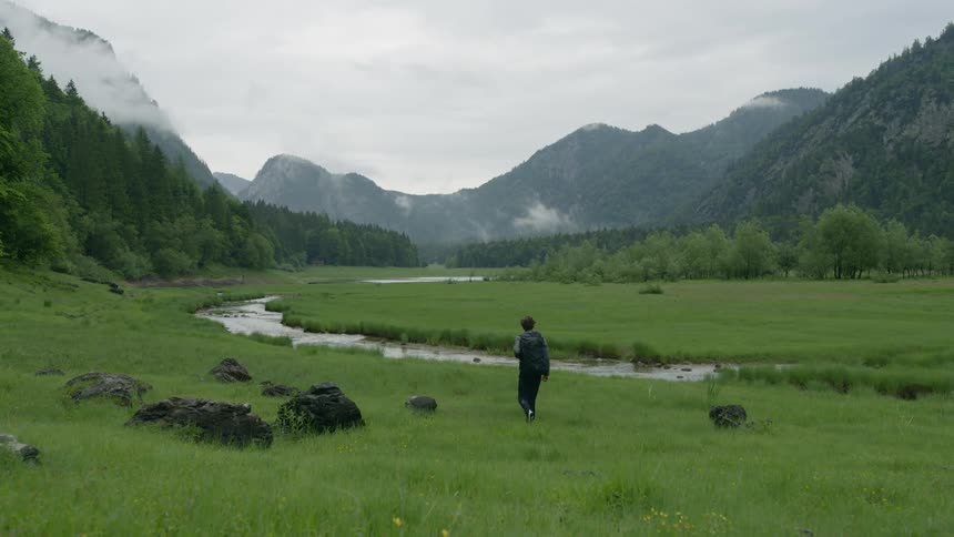 Man walking alongside a creek on a field in a valley