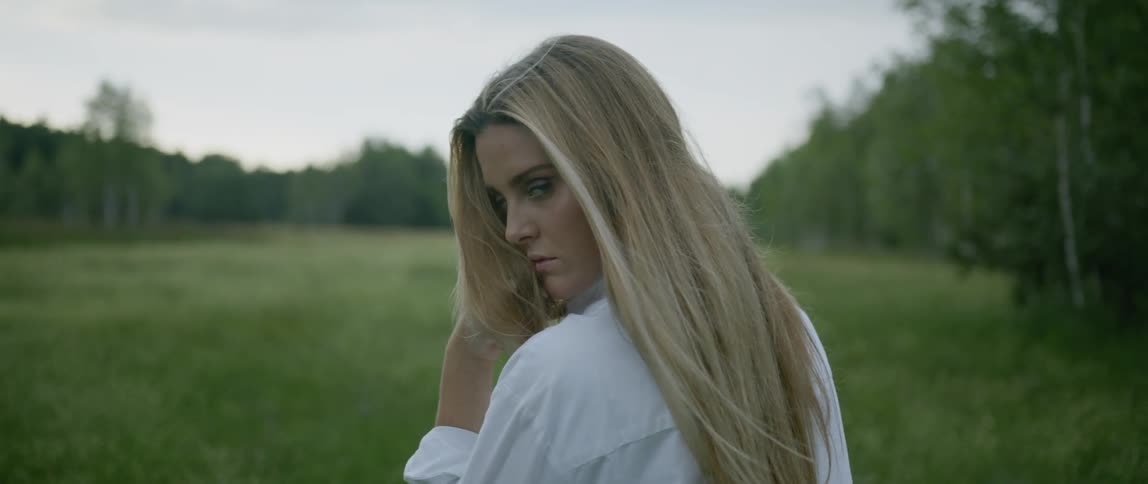 Blonde woman stands in the green field on a cloudy day