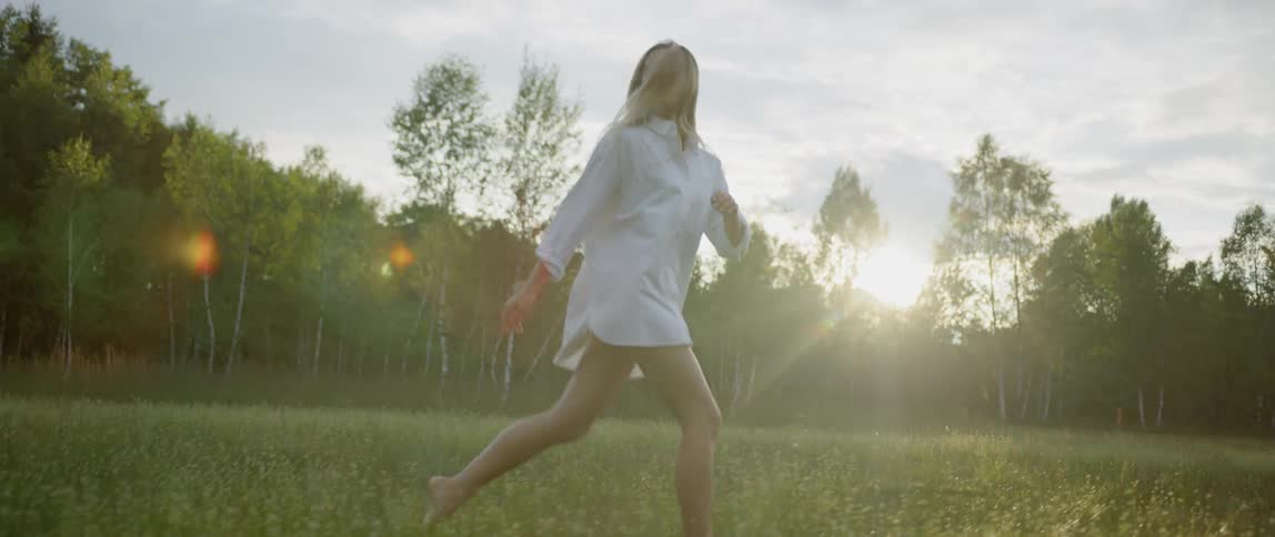 Woman wearing white shirt runs on the green grass at sunset