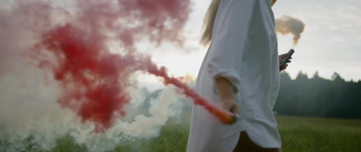 A young woman runs along while holding tubes that colored powder flows out of
