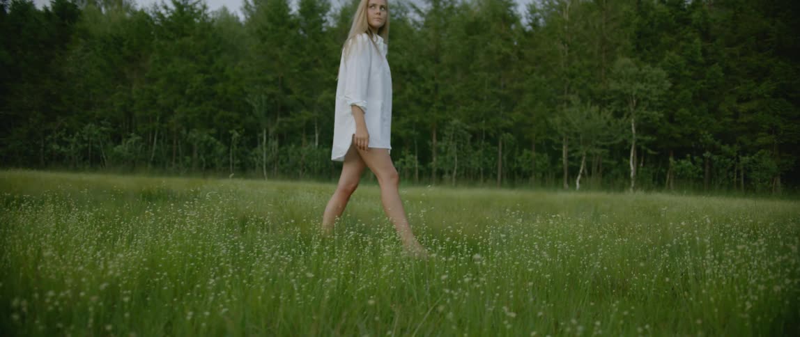 A woman with white shirt walking in the grass field