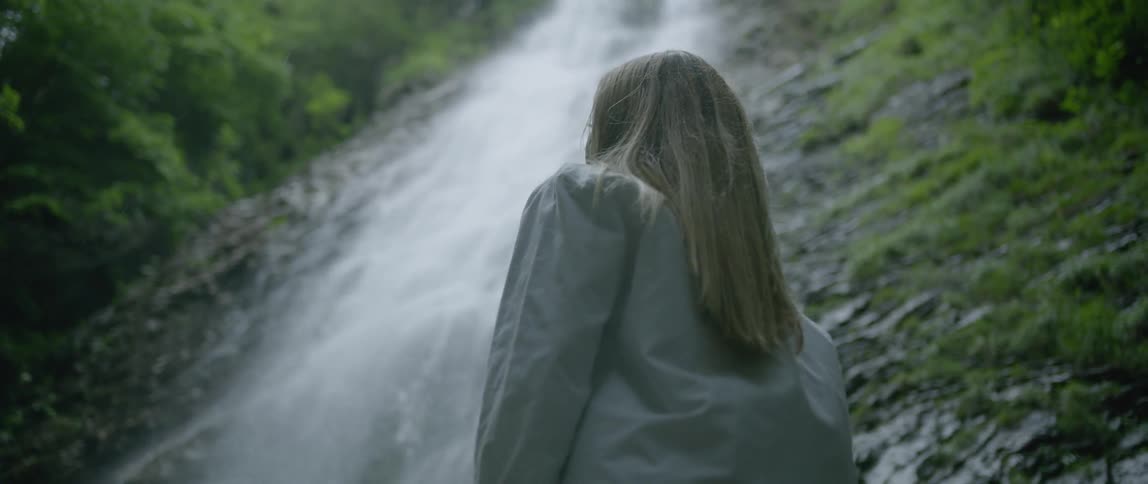 Woman looks up at waterfall in the woods during daylight