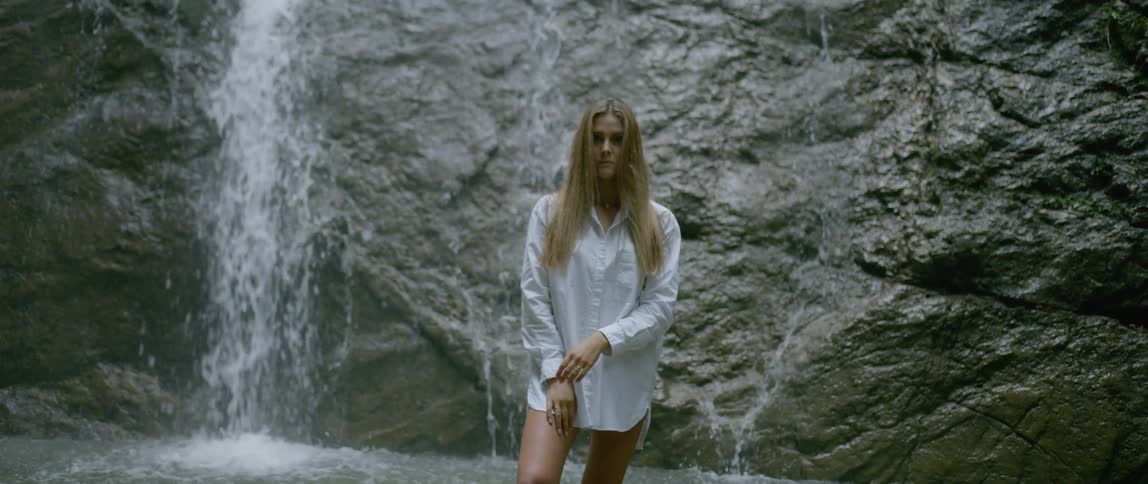 A woman with white shirt in front of a waterfall