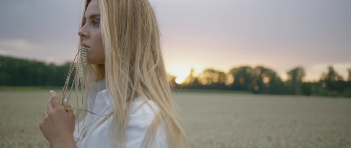 Woman stands in field at sunset holding wheat stalk