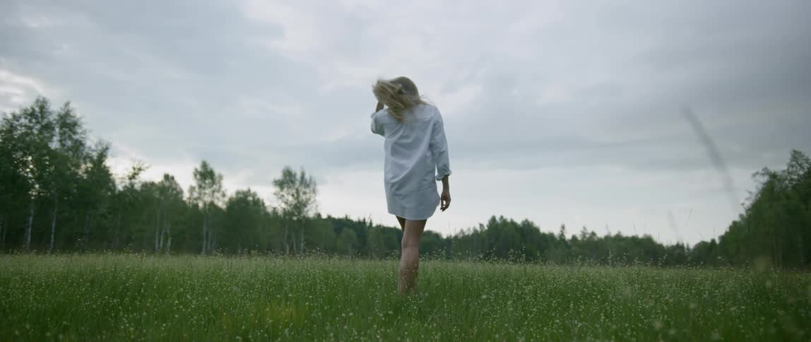 Blonde woman wearing a white shirt walks in the green field on a cloudy day