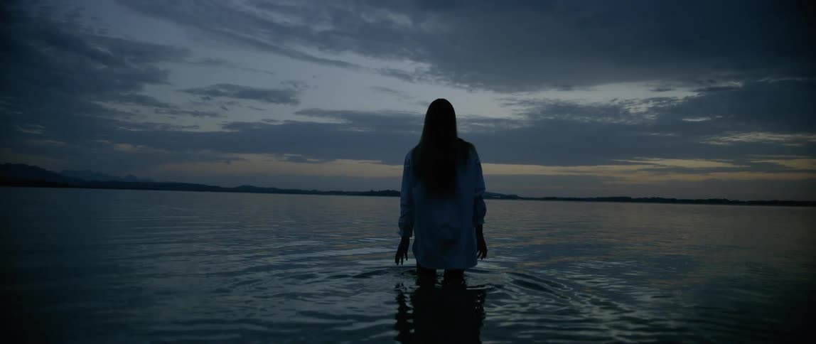 A woman with white shirt walking towards the ocean