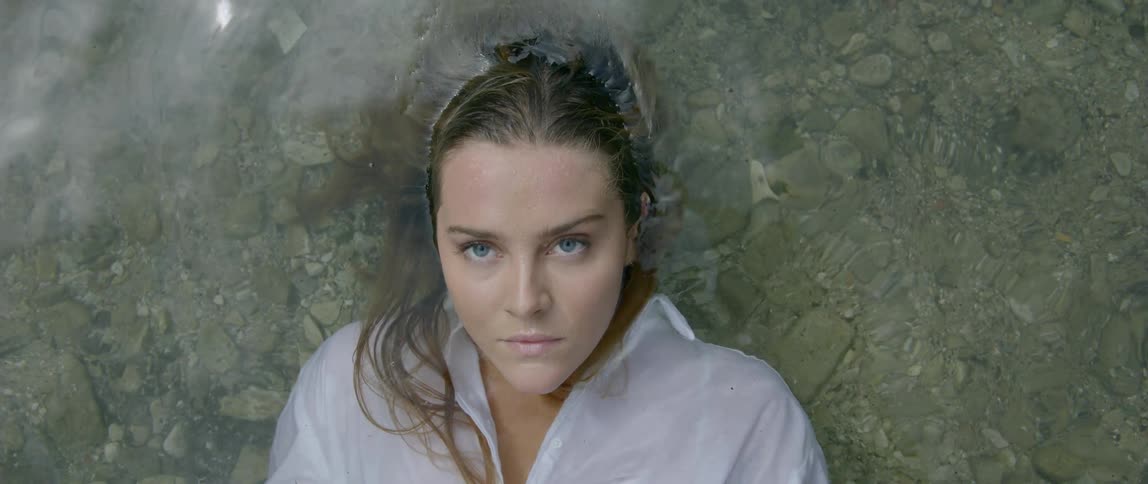 A young girl lies down in a creek in her clothes