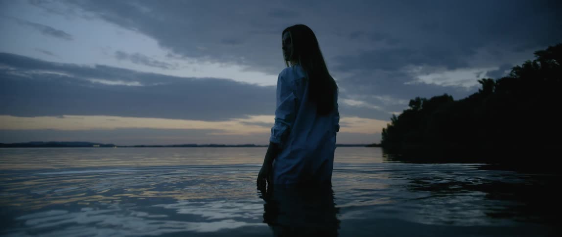 Woman fully clothed standing in water at the beach at sunset