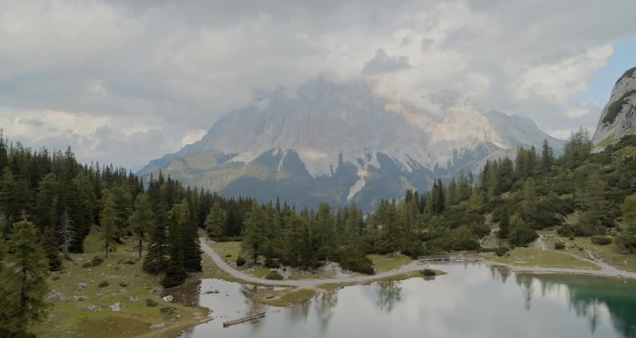 Aerial view of lake surrounded by pines and nearby mountain range